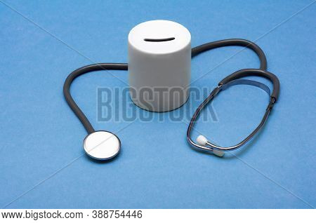 Cost Of Healthcare. Money Box With A Medical Doctors Stethoscope On Blue Background.