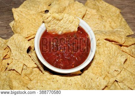 Top View Of Picante Sauce In A White Bowl Surrounded By Tortilla Chips On A Wood Table.