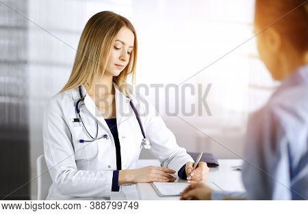 Young Beautiful Woman-doctor And Her Patient Are Discussing Patients Current Health Examination, Whi
