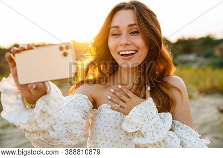 Young caucasian attractive brunette woman smiling and taking selfie phoro on cellphone outdoors