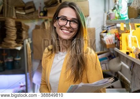 Successful Small Business Owner In Casual Wearing Yellow Cardigan, Standing In Her Store, Looking At