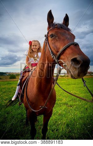 Girl In Nice Gypsy Dress With Sorrel Horse In A Field With Green Grass And Sky With Clouds In Backgr