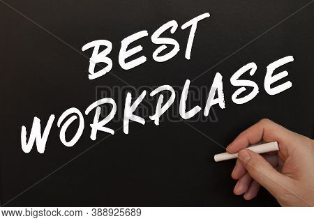 Male Hand Is Writing Best Workplase Words On Black Chalkboard. Drawn In Chalk In A Mans Hand. Busine