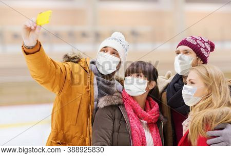people, friendship, technology and leisure concept - friends wearing face protective medical masks for protection from virus disease taking selfie with smartphone on skating rink