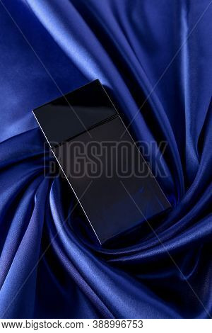 Perfume Bottle On Silk Folded Fabric Background. Glass Flask With Dark Blue Liquid.scent Fragrance C