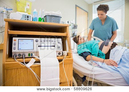 Test report coming out from ctg machine with nurse examining pregnant woman in background
