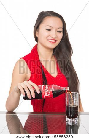 NAKHODKA, RUSSIA - JANUARY 18, 2014: Cheerful Asian girl pours a Coca-Cola from a bottle into a glass. Coca-Cola is a carbonated soft drink sold in stores, restaurants, and vending machines worldwide 