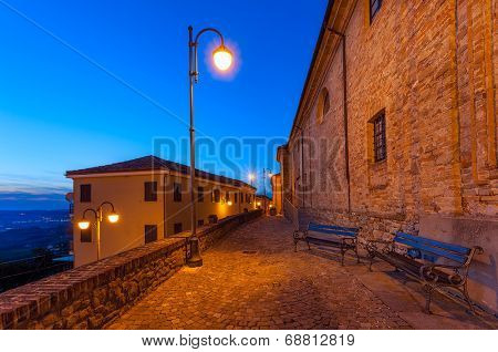 Benches on narrow illuminated cobbled street early in the morning in small italian town.