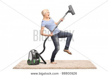 Young excited woman cleaning with a vacuum cleaner and pretending to be playing guitar on the hose isolated on white background