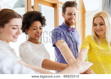 business, startup, gesture, people and teamwork concept - happy creative team with hands on top of each other in office