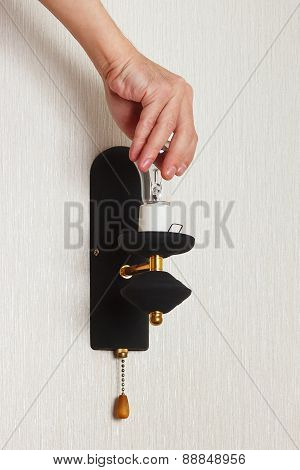 Hand twists bulb in a lamp on white wall