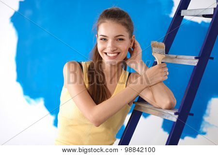 Beautiful young woman doing wall painting, standing near ladder