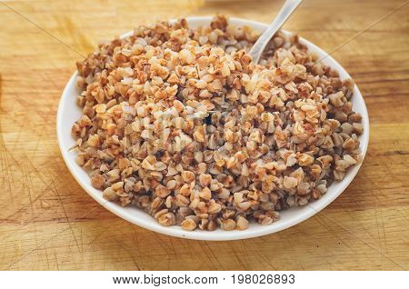 buckwheat porridge in white ceramic plate on vintage wooden table
