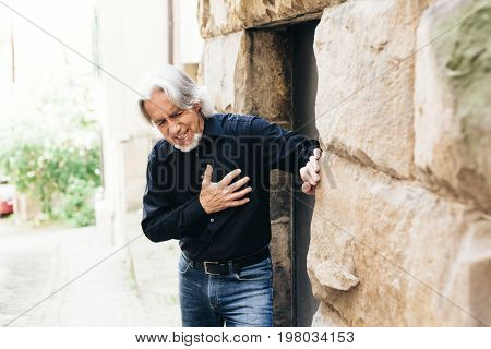 Senior walking through city, having heart attack