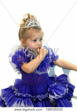 Little pageant girl fearfully sucks her thumb. She is wearing a tiara and wearing a fancy purple pageant dress.