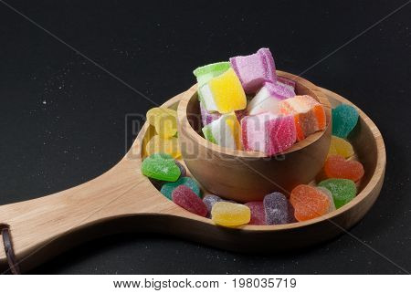 Multicolored jelly in a wooden cup against a black background.