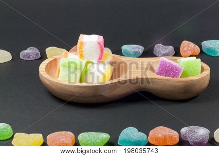 Multicolored jelly in a wooden cup against a black background.