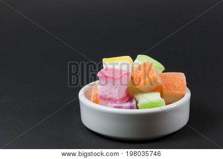 Multi-colored jelly in a white tile cup against a black background.