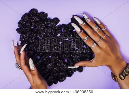 woman hands with long nails manicure holding fruits in shape of heart on purple background close up