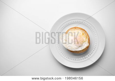 Ceramic plate with hamburger roll and over hard fried egg on light background
