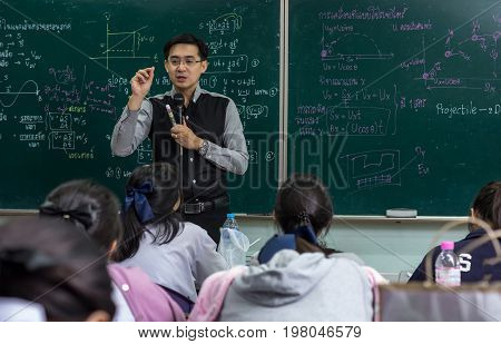 Asian teacher Giving Lesson to group of College Students which answer the question in the classroom over the physics formular in thai laguage on black board school education concept