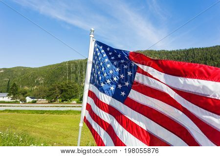 Flag of the United States of America (American flag or The Stars and Stripes Old Glory The Star-Spangled Banner) waving in the wind against summer forest landscape in sunny day.