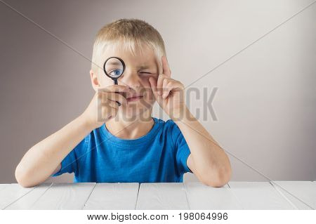 Curious boy with a clever face looks through the magnifying glass and lifts his index finger up. The concept of logical thinking.