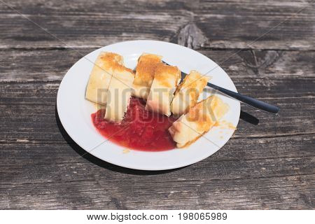 Traditional Slovene Struklji with strawberry jam an white plate, wood as background. Struklji are made of cooked dough and cottage cheese and can be served as side dish or dessert