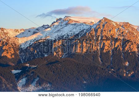 Fantastic view in winter season with the peak of Bucegi massif in the warm colorful sunset light landscape seen from resort Fundata Cheile Gradistei Romania.