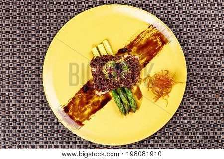 Quinoa crusted fish on asparagus on yellow plate on Wicker place mat