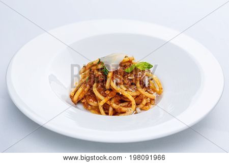Pasta with tomato sauce and parmesan in white plate on white tablecloth.