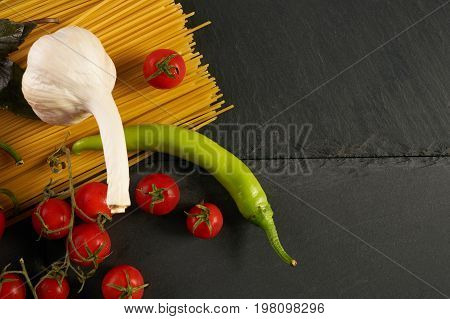 Food preparation fresh vegetables tomatoes bell pepper garlic basil and spaghetti on black slate plate. Raw ingredients for cooking traditional italian pasta. Closeup top view copy space