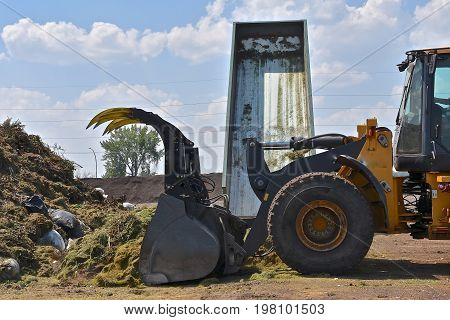 As a truck hydraulic  box loads a load of grass trimmings, a front end loader pushes it into a compost pile.