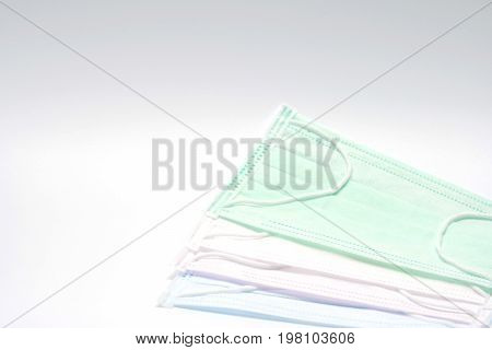 Green pink light blue and white ear loop disposable face mask overlapping used for covering mouth and nose. It protects against body fluid and large particles in the air