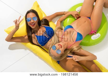 Sexy girls wearing sunglasses and blue bicinis lying on yellow swimming air mattress shot from above isolated