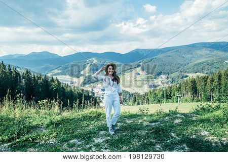 young pretty woman in hat walking by mountain peak