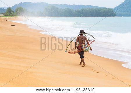 local Phuket fisherman walking home along a Phuket beach from fishing on an early morning day carrying his primitive fishing tools