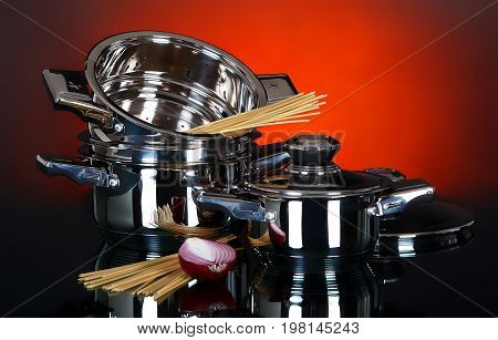 Empty pots and pans with raw vegetables and pasta on a dark background