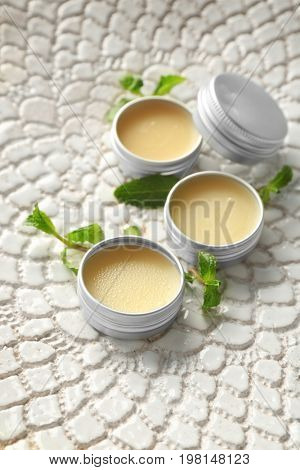 Containers with lemon balm salve and leaves on textured surface