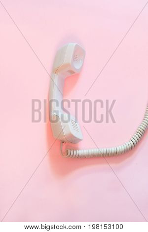 Top view of white telephone handset/ receiver and cord isolated on pink background.