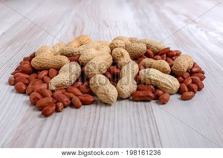A heap of unpeeled and peeled peanuts on a light kitchen table close-up.