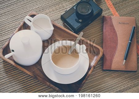 Vintage Film Look: cup of coffee with camera and notebook on mat abstract background