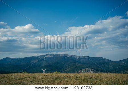 woman in field with mountains on background pictered from long distance in summer day
