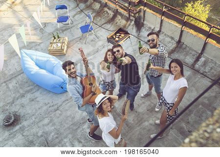 Top view of a group of young friends having fun at a rooftop party playing the guitar singing and enjoying hot summer days. Focus on the people in the middle