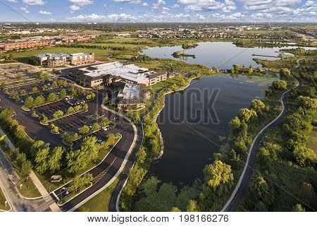 Aerial view of a lake beside a community center and grade school with walking paths and bridge at The Glen in Glenview, Illinois.