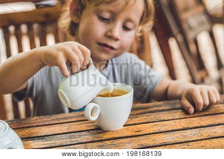 Happy Nice Boy Pours Honey Into The Tea In Summer Green Garden. Portrait. Outdoor