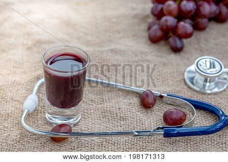 Purple grapes, grape juice in a red heart glass and heart detectors are placed on brownish-gray sackcloth.