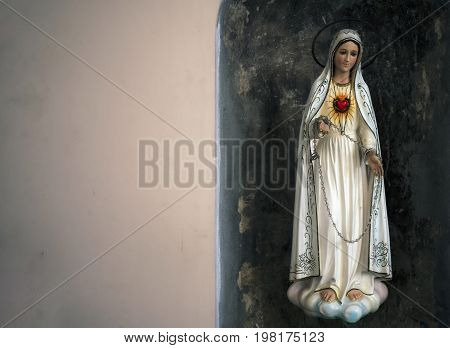 The figure of the Virgin Mary in white robes on which the scarlet heart in the crown shines stands on the cloud.