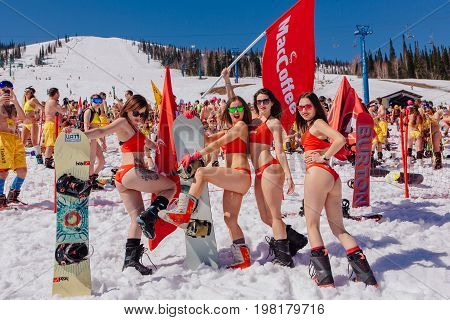 Sheregesh, Kemerovo region, Russia - April 22, 2017: Grelka Fest is a sports and entertainment activity for ski and snowboard riders in bikini in Russia, Sheregesh. Group of young happy pretty women on a snowboard in colorful bikini with flags.