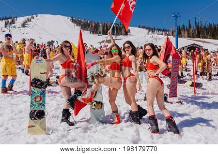 Sheregesh, Kemerovo region, Russia - April 22, 2017: Grelka Fest is a sports and entertainment activity for ski and snowboard riders in bikini in Russia, Sheregesh. Group of young happy pretty women on a snowboard in colorful bikini with flags.